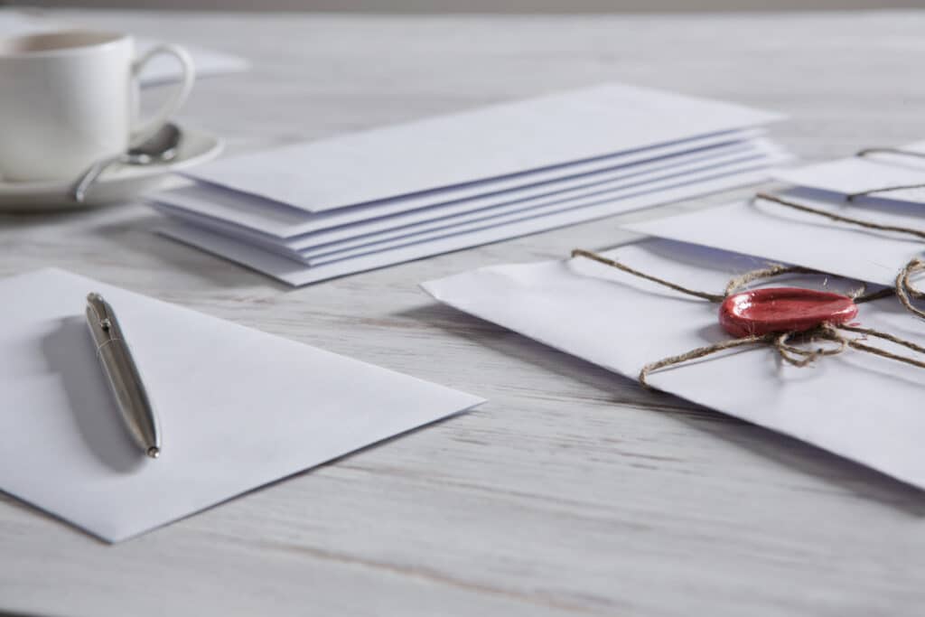 Old post concept with envelope with wax seal and blank paper sheets on wooden surface