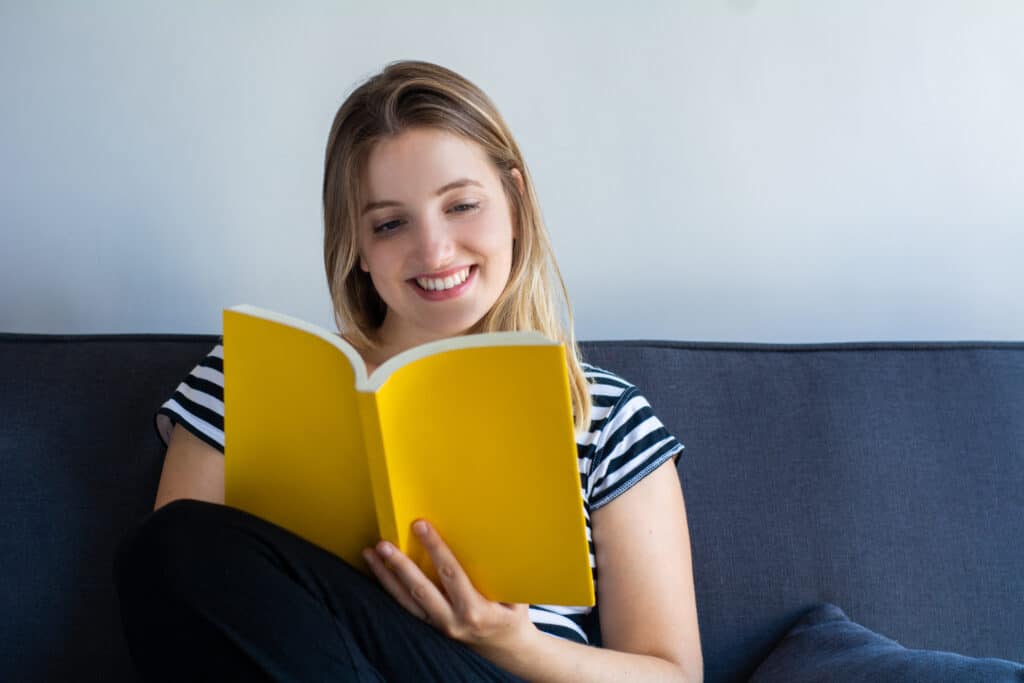 Young woman reading a book and lying on sofa at home.